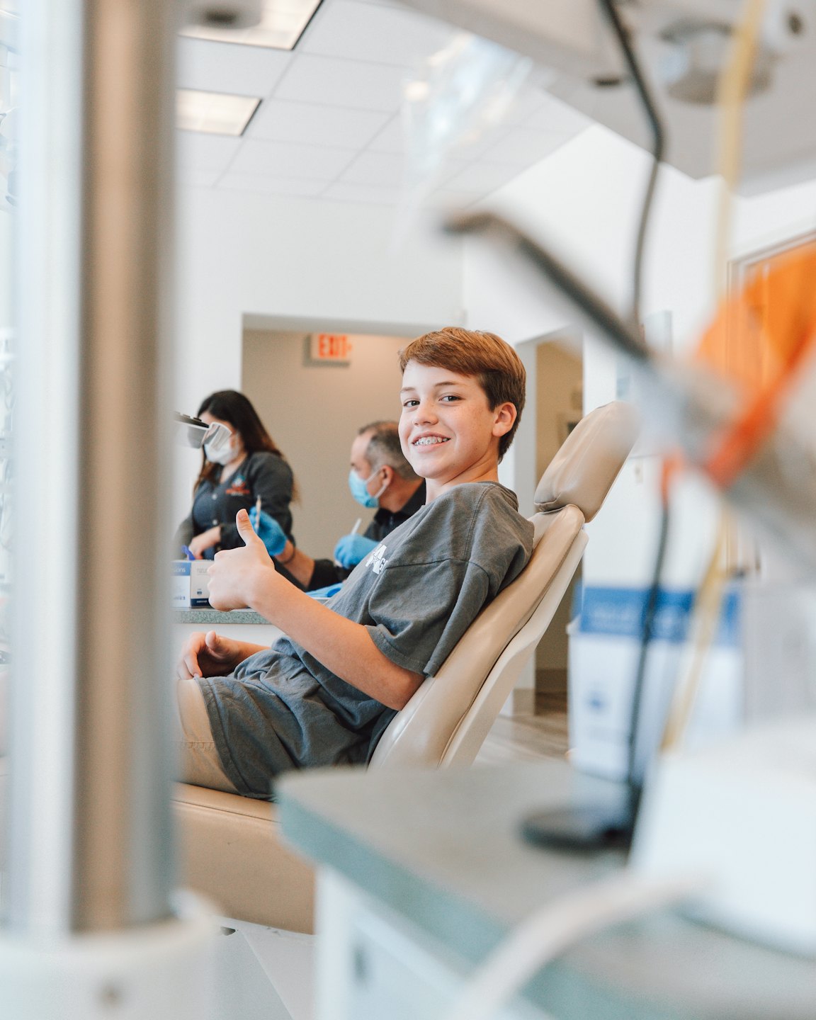 Smiling boy gives thumbs up in a dental chair.