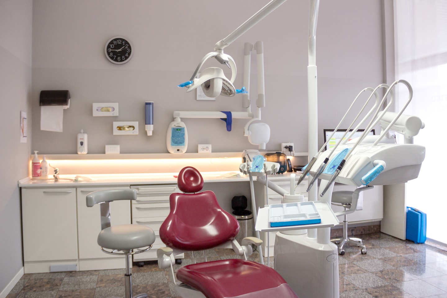 Modern dentist's office with red chair and medical instruments.