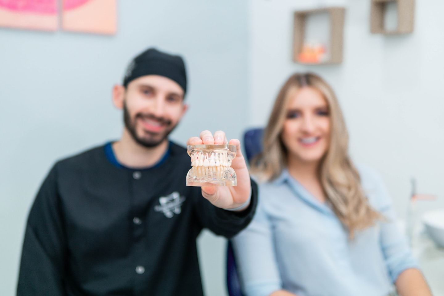 A smiling dentist holds a dental model in a bright office.